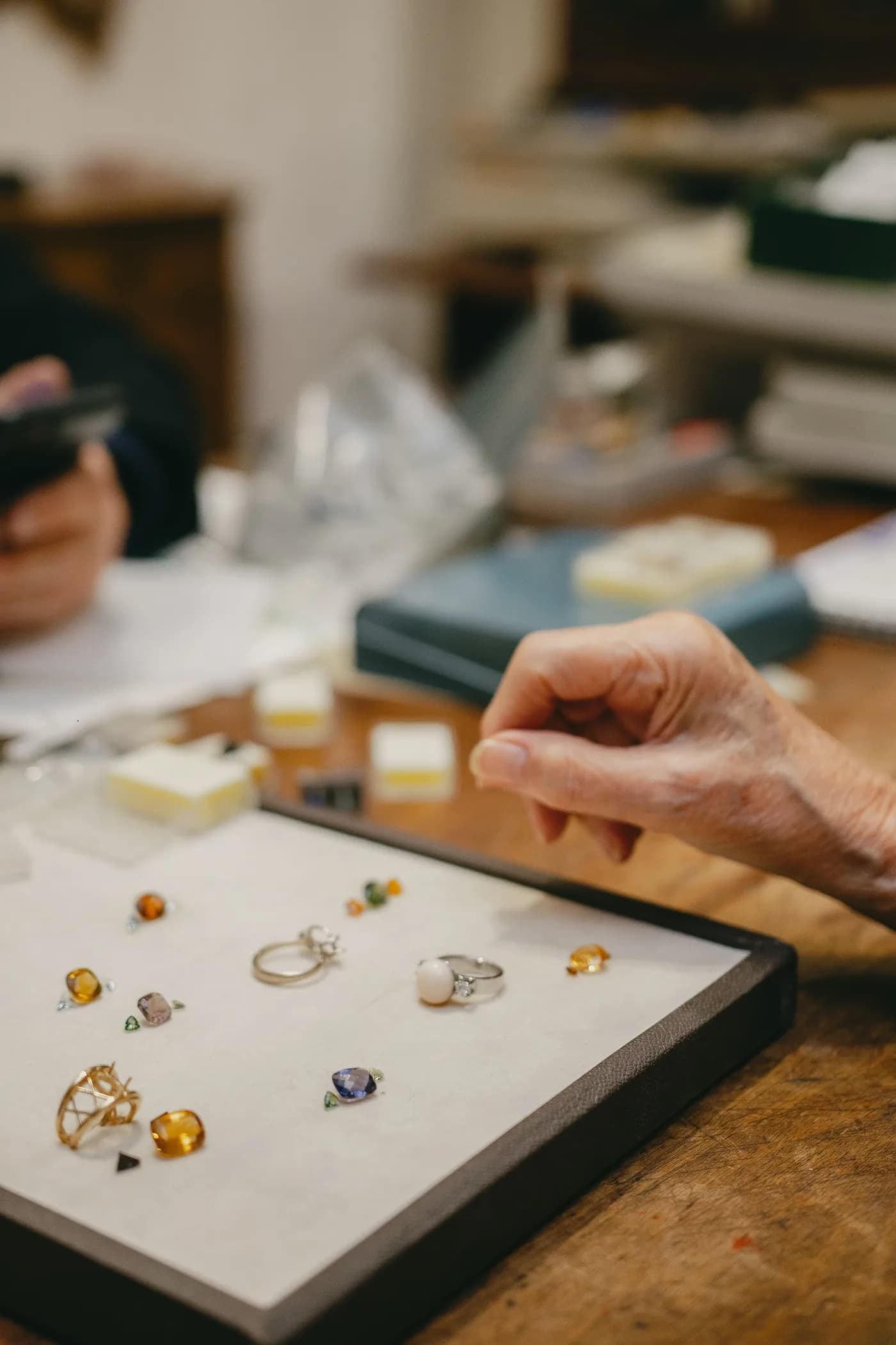 A hand choosing from rings and loose stones laid out on a tray on the shop counter