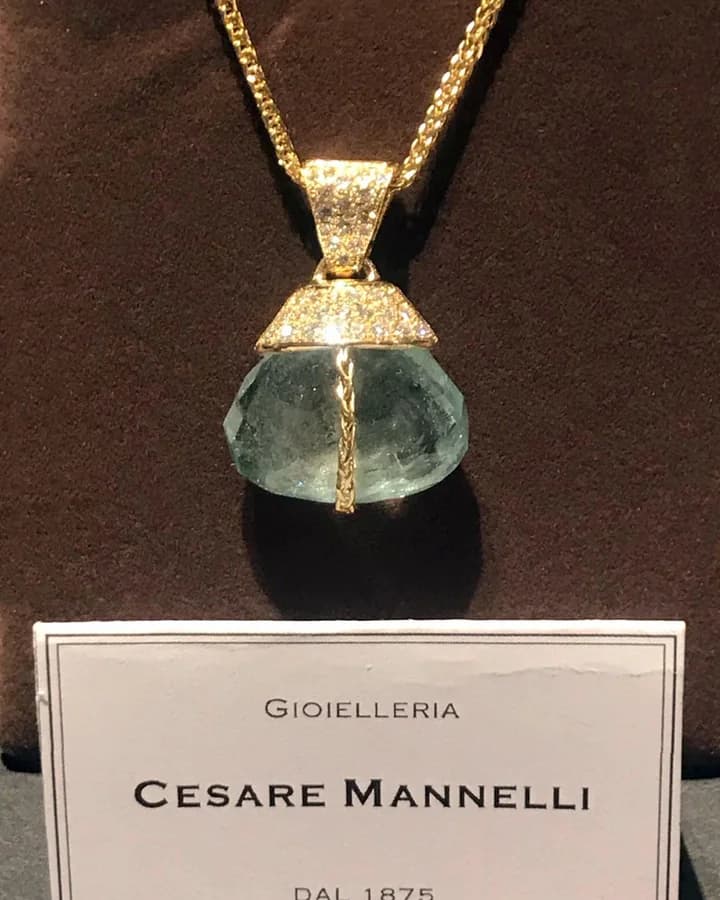 A pendant with a large pale faceted stone on a chain, displayed in front of the card reading Gioielleria Cesare Mannelli dal 1875