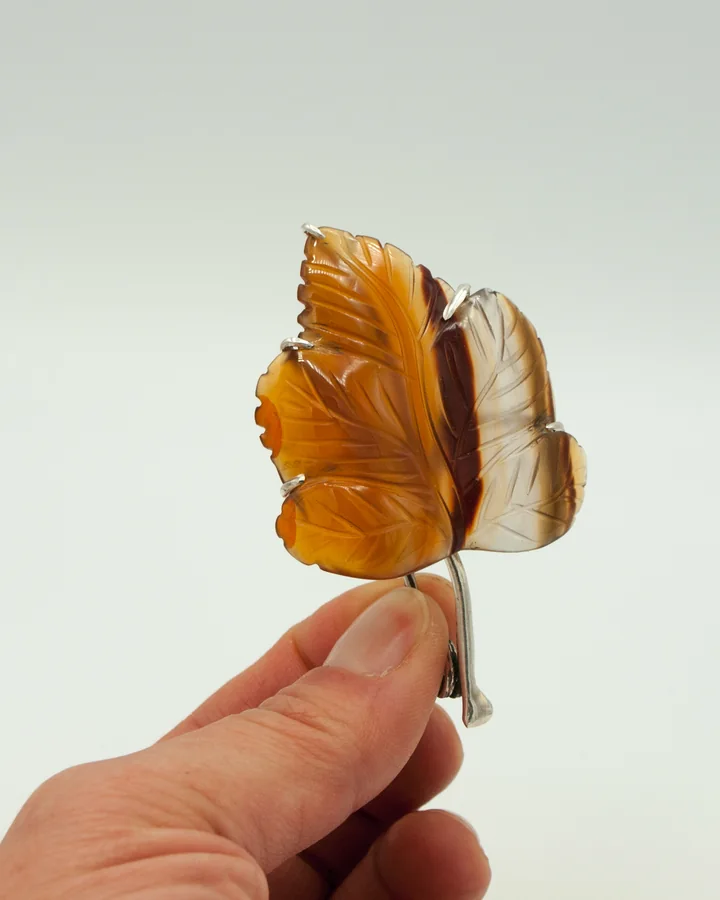 A leaf carved from stone, with amber veining, held between two fingers